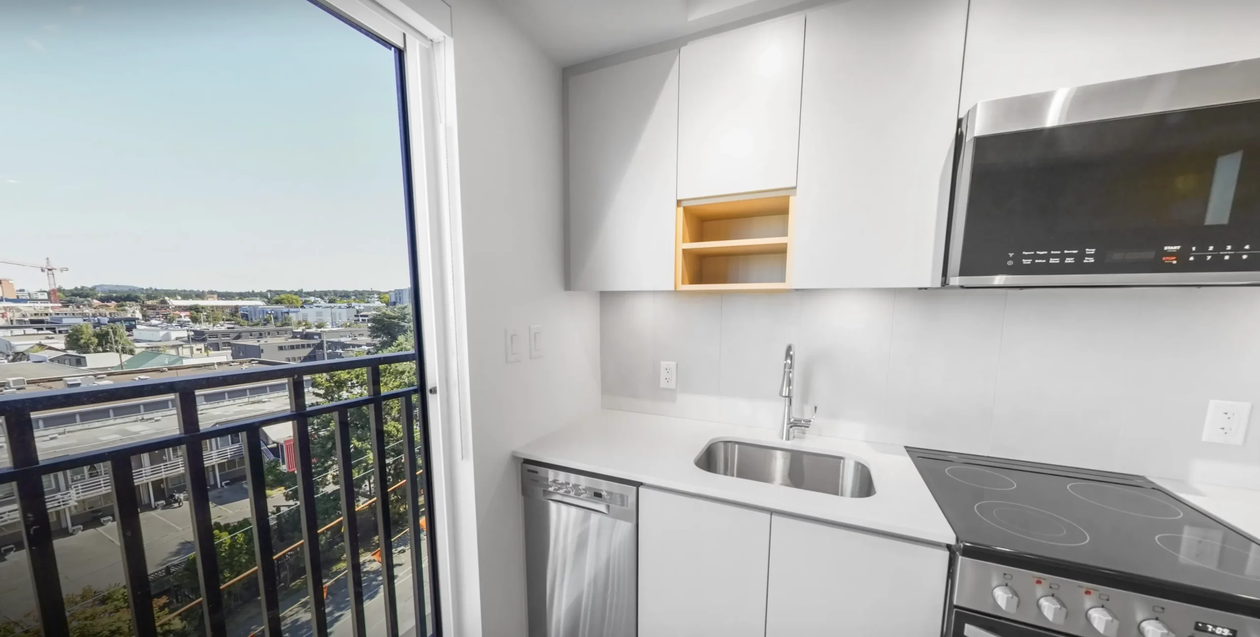 Bright kitchen with white cabinetry and countertops and stainless steel appliances in a Spencer Block rental home, with a juliette balcony to the left